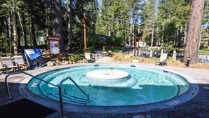 A hot tub surrounded by lounge chairs and a wooden deck, set in a wooded area with a spa capacity sign. - 3178 Aspen Grove (Truckee)