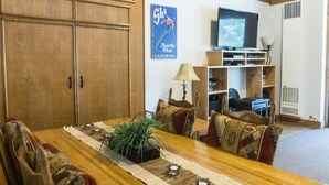 A living room with a wooden dining table, chairs, a television, and a bookshelf. - 3178 Aspen Grove (Truckee)