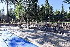 A pool area with lounge chairs and umbrellas, surrounded by trees.