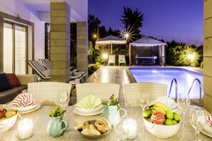 A poolside dining area with wicker furniture, a pool, and a covered seating area. - Villa Chiara (Kissonerga)