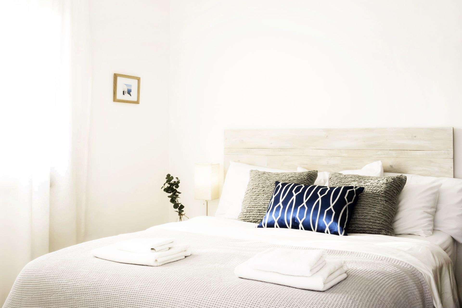 Una cama bien hecha con cabecera de madera, sábanas blancas y algunos cojines decorativos.