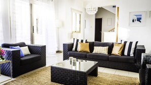 A modern living room with a black sofa set, a glass coffee table, and a woven rug. - Villa Chiara (Kissonerga)