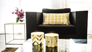 A modern living room with a black sofa, a patterned pillow, a vase with flowers, and two decorative candles on a glass table. - Villa Chiara (Kissonerga)