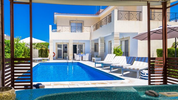 A modern pool area with a clear blue pool, lounge chairs, and a hot tub. - Villa Chiara (Kissonerga)