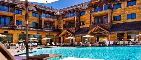 Un edificio de madera de varios pisos con piscina, asientos al aire libre y un patio cubierto.