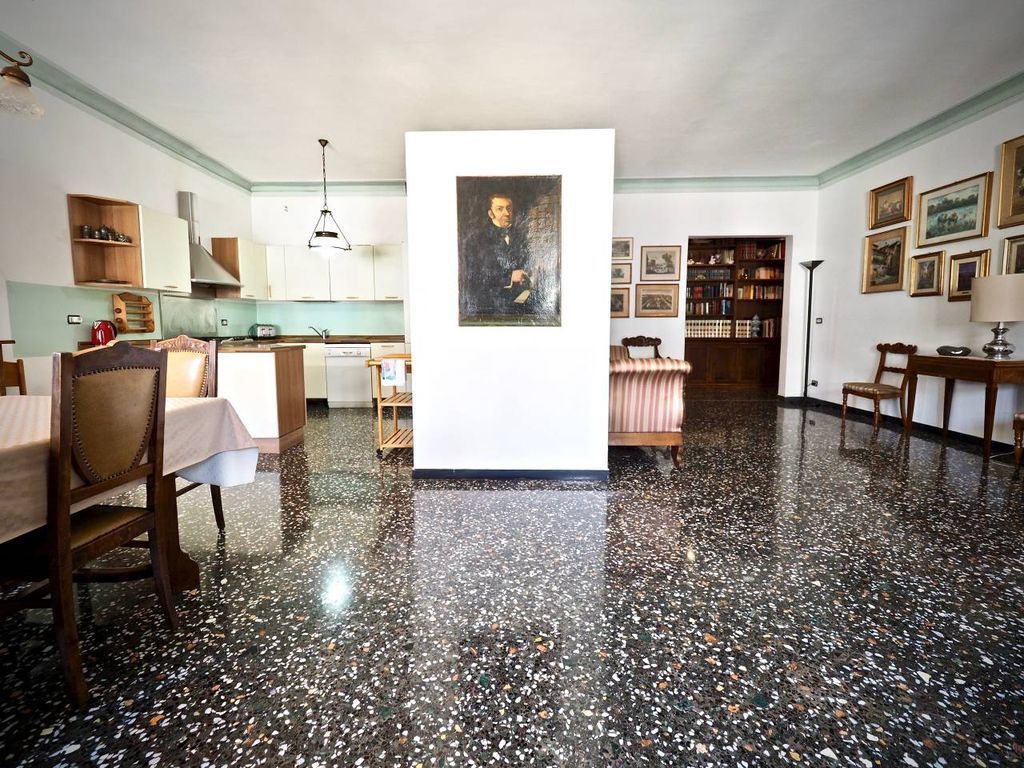 Een ruime kamer met een gepolijste vloer, een zithoek met een tafel en stoelen, een keuken met kasten en een spoelbak, en een boekenplank vol boeken.