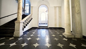 Un vaste hall orné de colonnes de marbre, doté d’un sol à motifs étoilés et d’un escalier avec une balustrade.