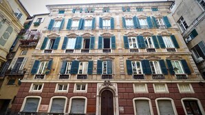 Il s’agit d’un bâtiment historique à étages, doté d’une entrée centrale surmontée d’un arc décoratif, de grandes fenêtres avec volets et de balcons.