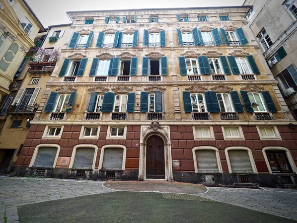 A historic building with multiple stories, featuring a central entrance with an ornate archway, large windows with shutters, and balconies.