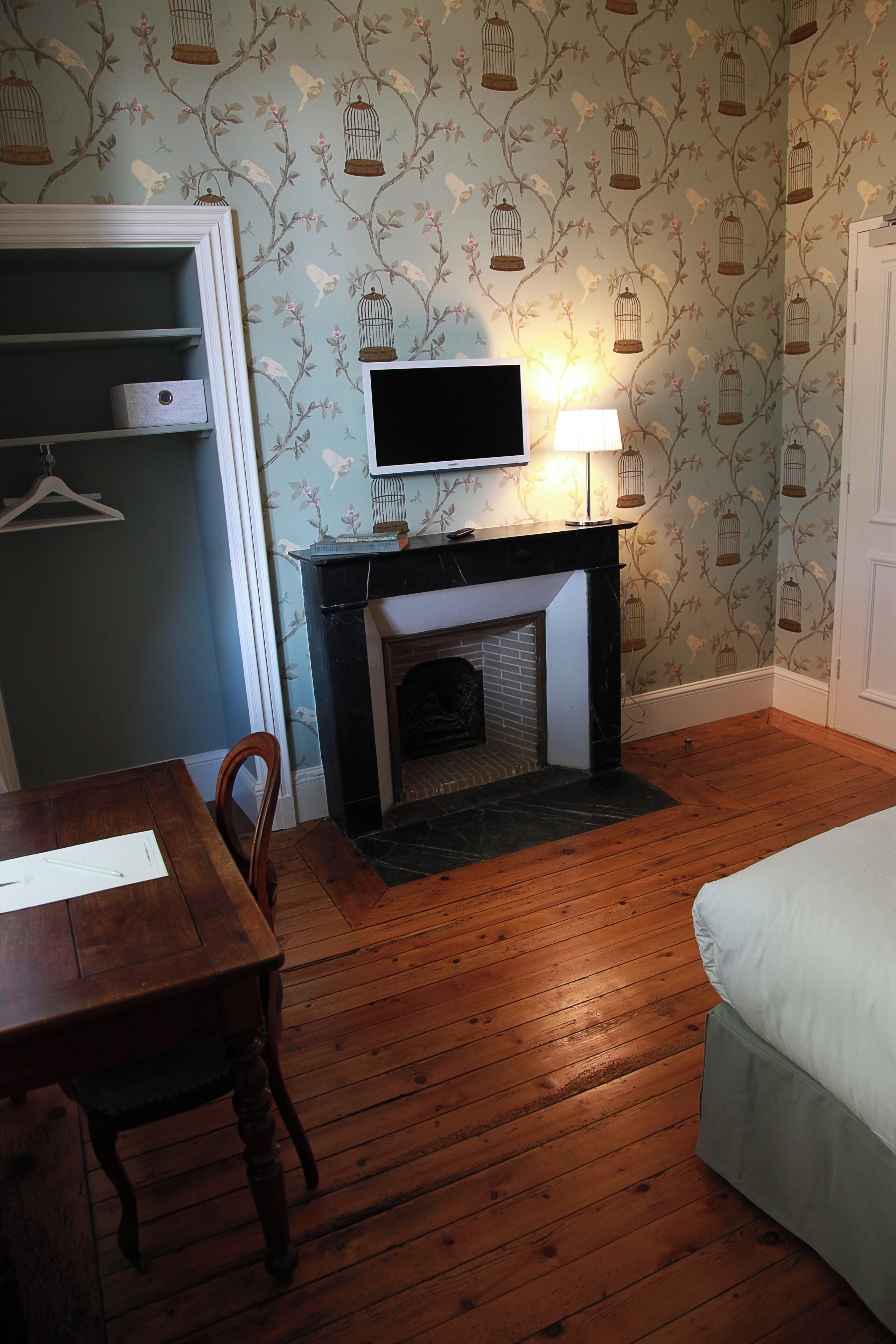 A room with a fireplace, a television mounted above it, a dining table with chairs, and a bed.