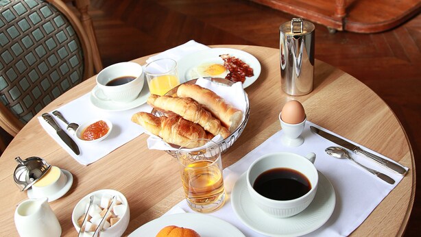 Una mesa de desayuno servida con cruasanes, jugo de naranja y café.