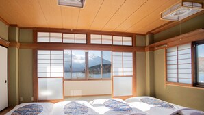 Une pièce de style japonais traditionnel, avec un sol recouvert de tatamis, des paravents en papier de riz (shoji) et un lit recouvert d’une courtepointe matelassée.