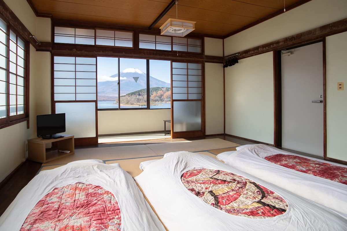 Ein traditioneller japanischer Raum mit Tatami-Bodenbelag, einem Fernseher auf einem niedrigen Tisch und Blick auf einen Berg.