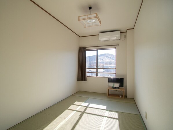 Een kamer met tatami vloerbedekking, een televisie op een houten standaard en een raam met uitzicht op een berg.
