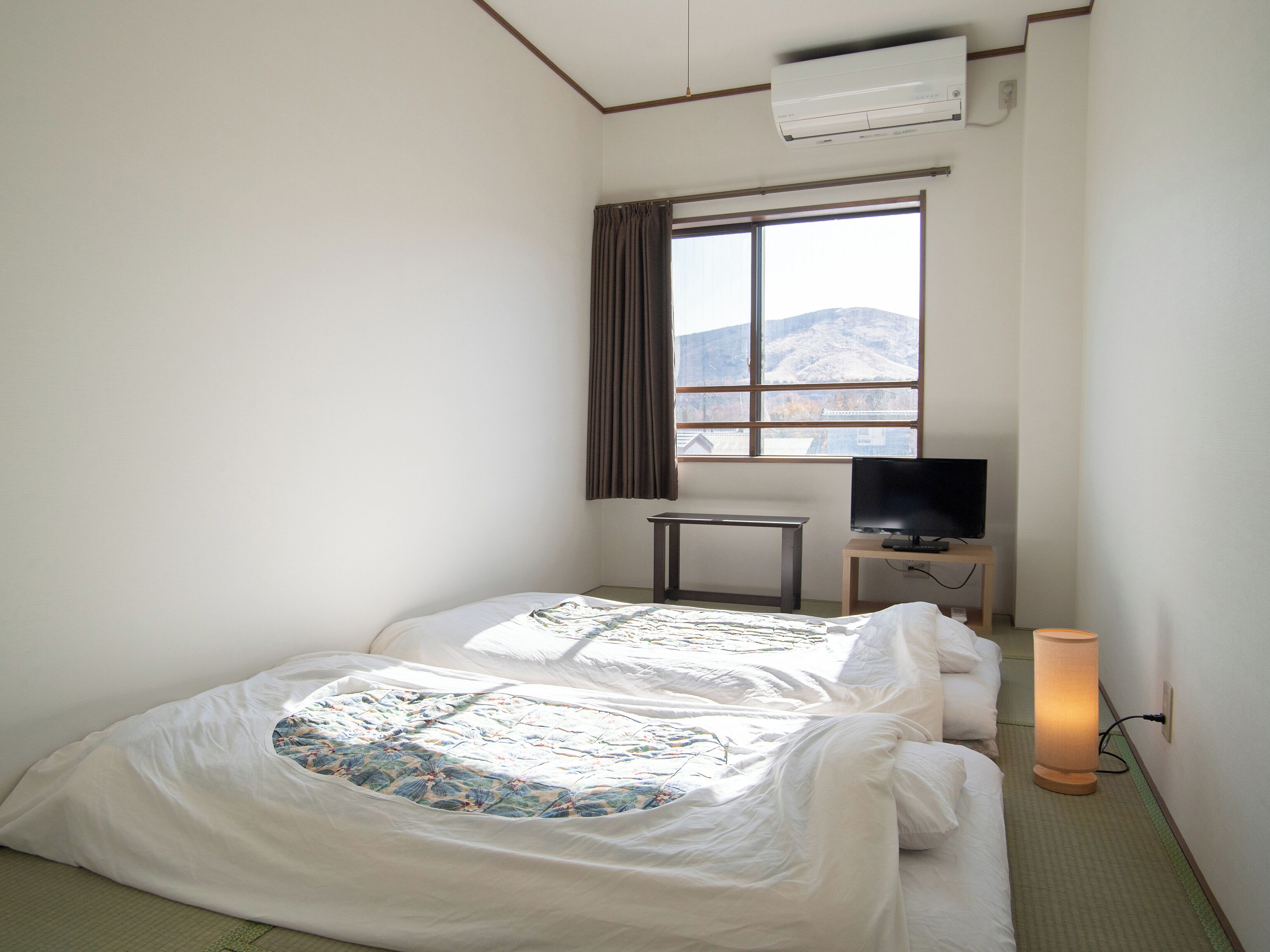 Quarto de hotel com cama, televisão, mesa de cabeceira e janela com vista para uma montanha.