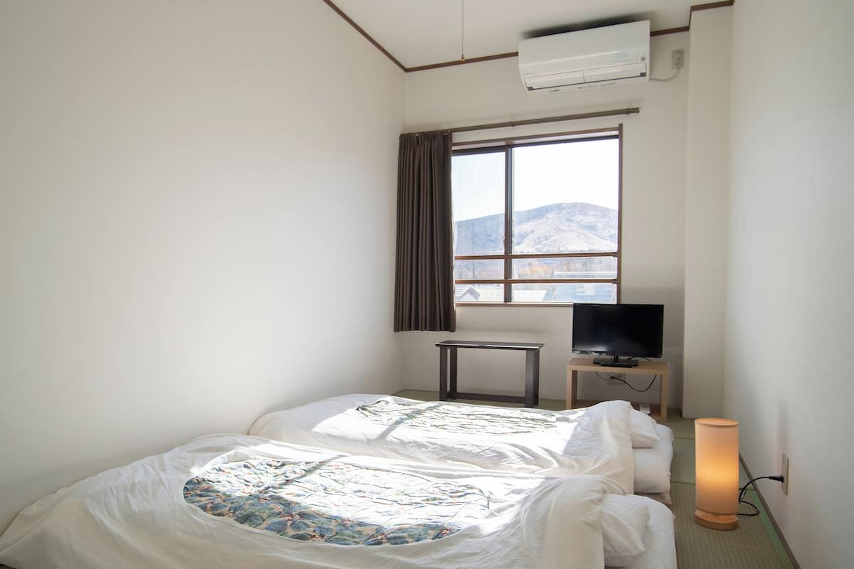 Ein Hotelzimmer mit einem Bett, einem Fernseher auf einem Schrank, einem Fenster mit Vorhängen und einer Klimaanlage.