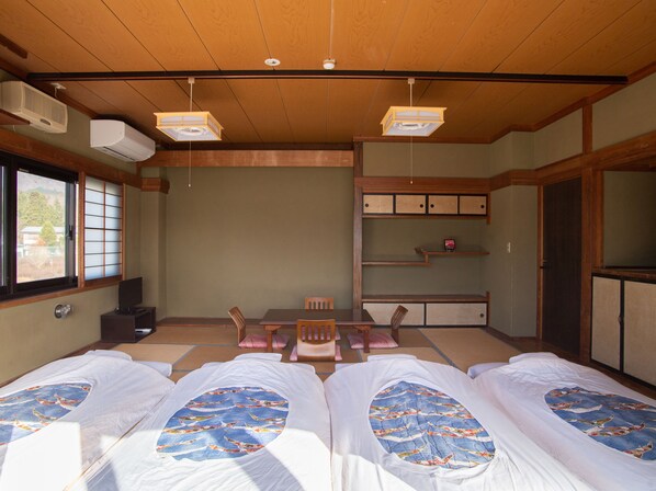 A traditional Japanese-style room with tatami flooring, a low table with chairs, and two beds with matching bedding. - Tabist Lakeside Inn Fujinami Yamanakako (Yamanakako)