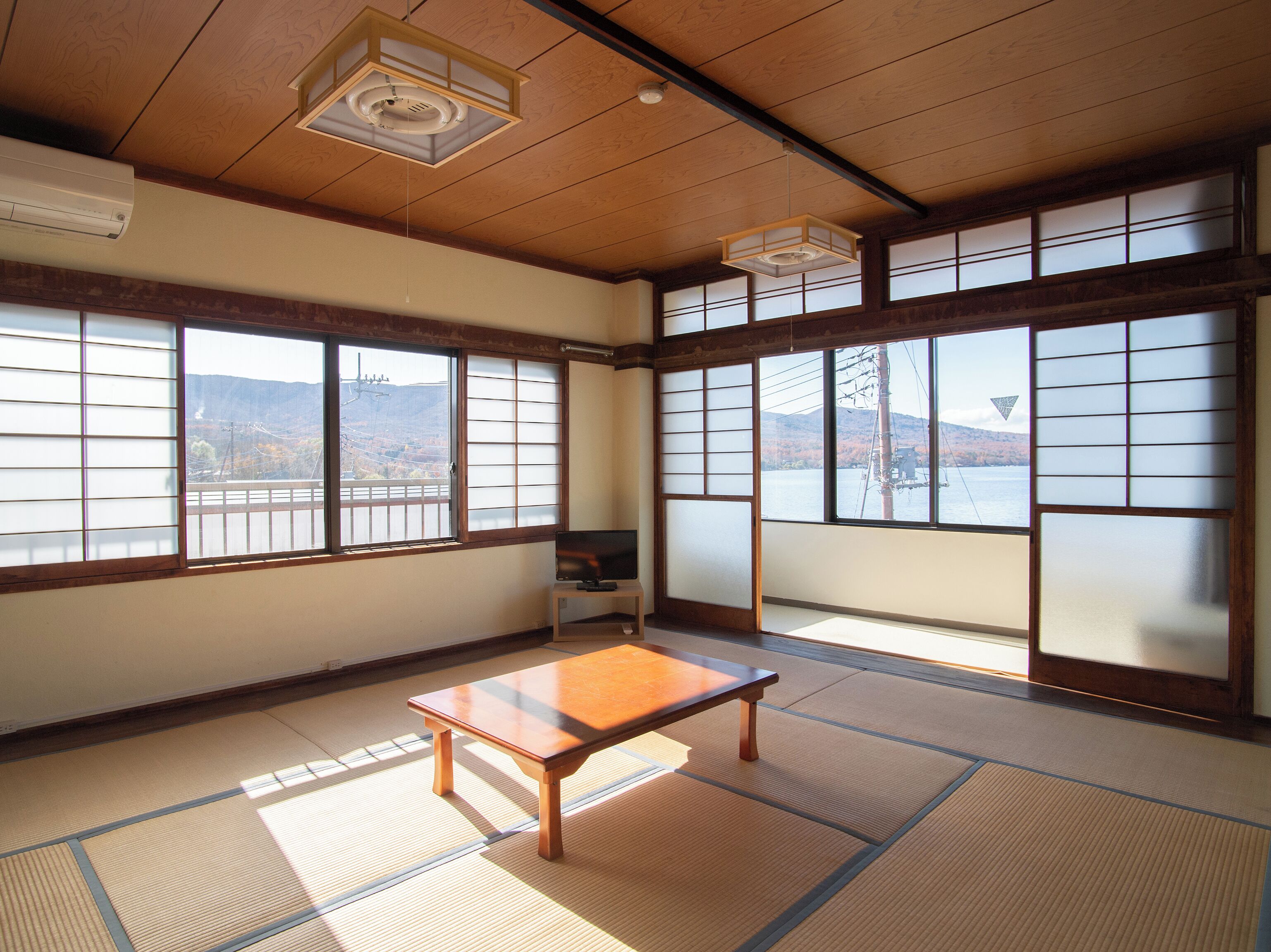 Um quarto japonês tradicional com tatames, portas deslizantes shoji e vista para uma paisagem montanhosa.