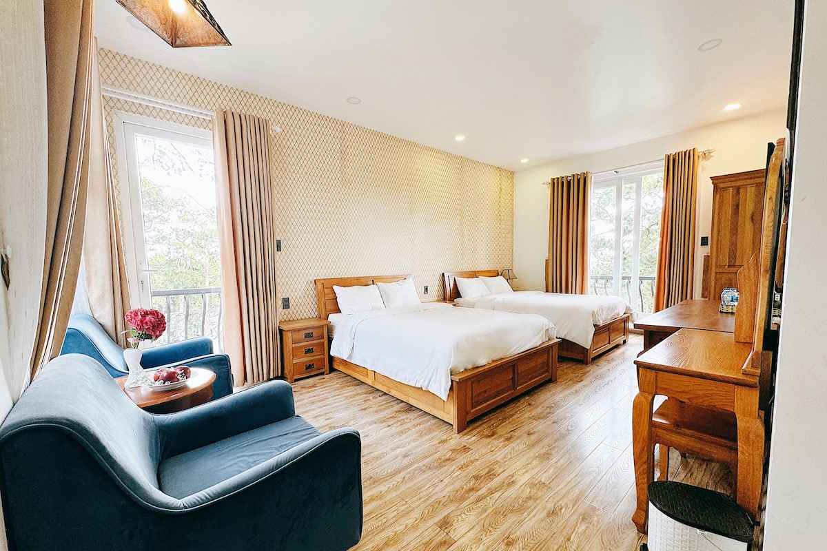 Habitación de hotel con dos camas, un sofá, un escritorio de madera y vistas al exterior.