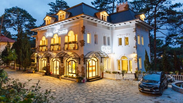 A large, two-story building with a sign reading "Joy Villa." It features a stone-paved courtyard, multiple arched windows, and a car parked in front. - TTR Joy Apart Hotel (Xuan Huong - Da Lat)