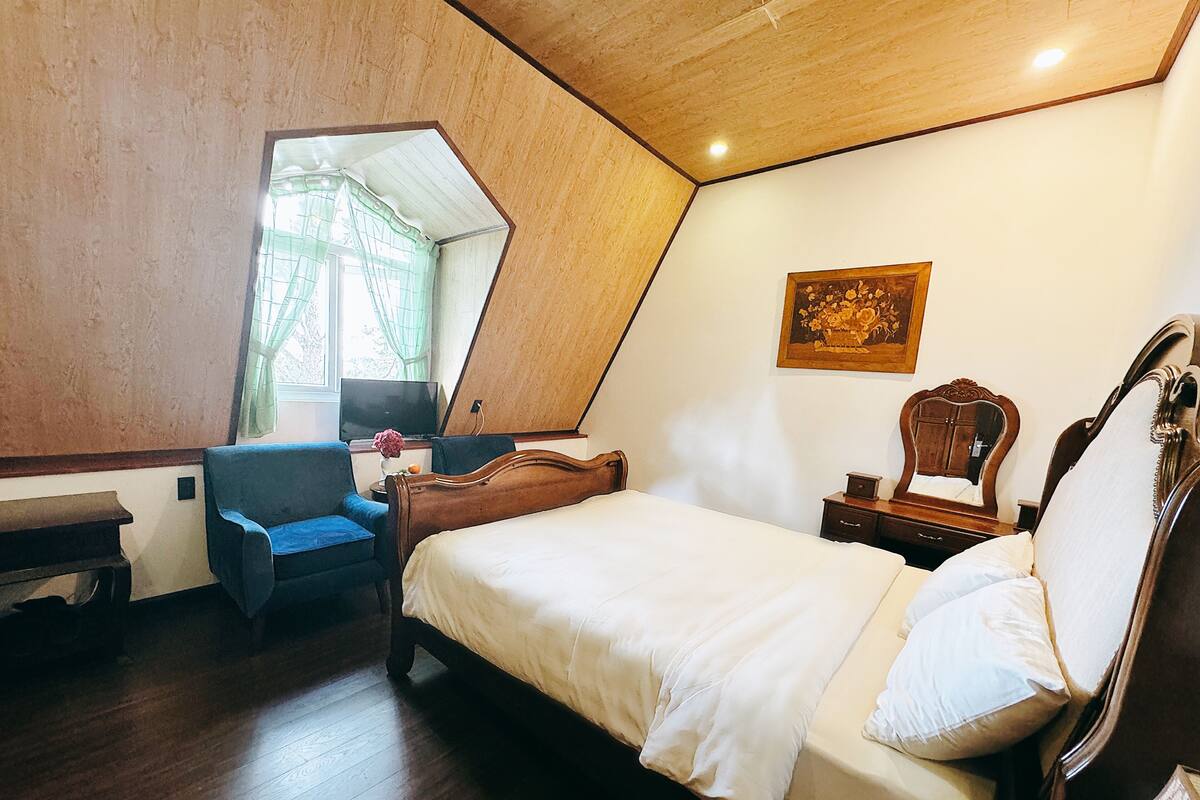 Un dormitorio con cama, escritorio, silla, televisor y ventana con cortinas.