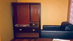 Una habitación pequeña con un armario de madera, un sofá de cuero negro y una mesa de madera con un periódico.