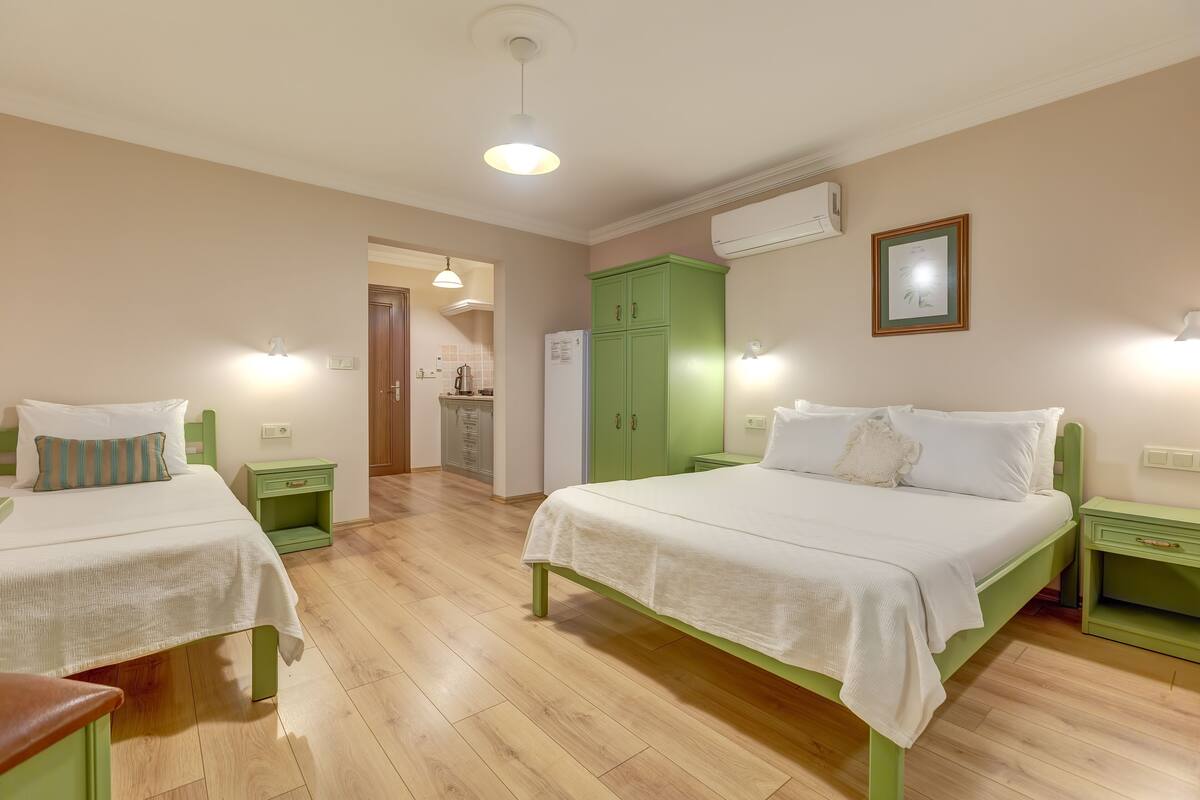 Un dormitorio con dos camas, un armario verde, una pequeña cocina y un equipo de aire acondicionado.