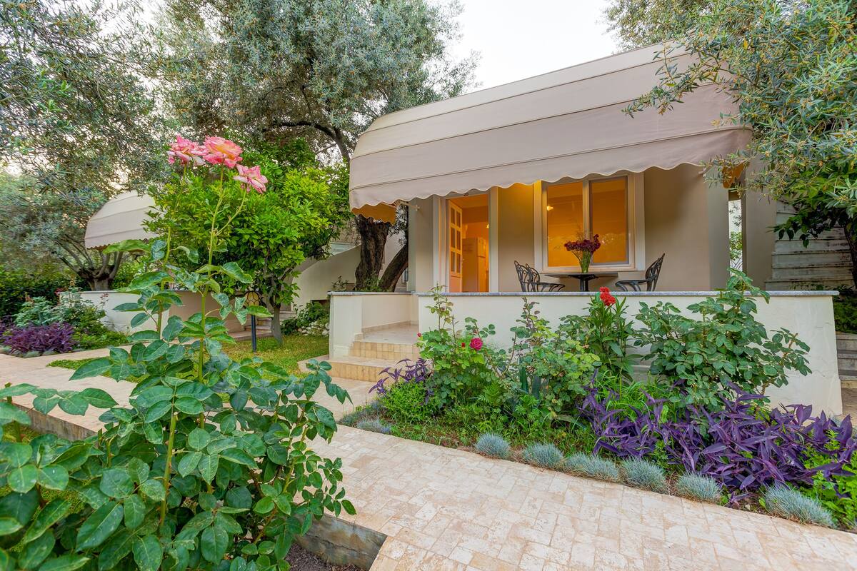 Una casa moderna con un porche cubierto, un jardín con diversas plantas y una escalera que conduce a la entrada.
