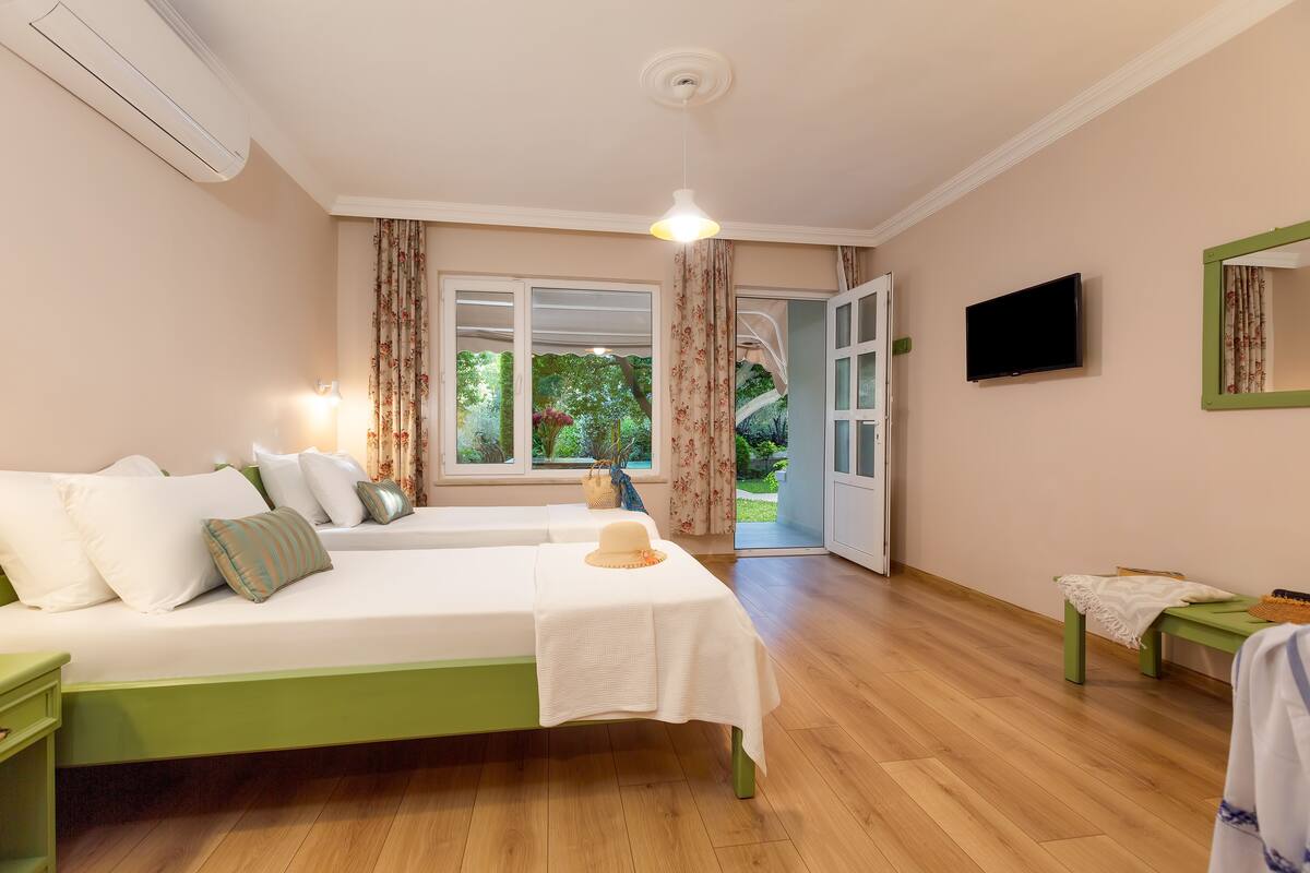Habitación de hotel con dos camas, televisión, espejo y vistas al jardín.