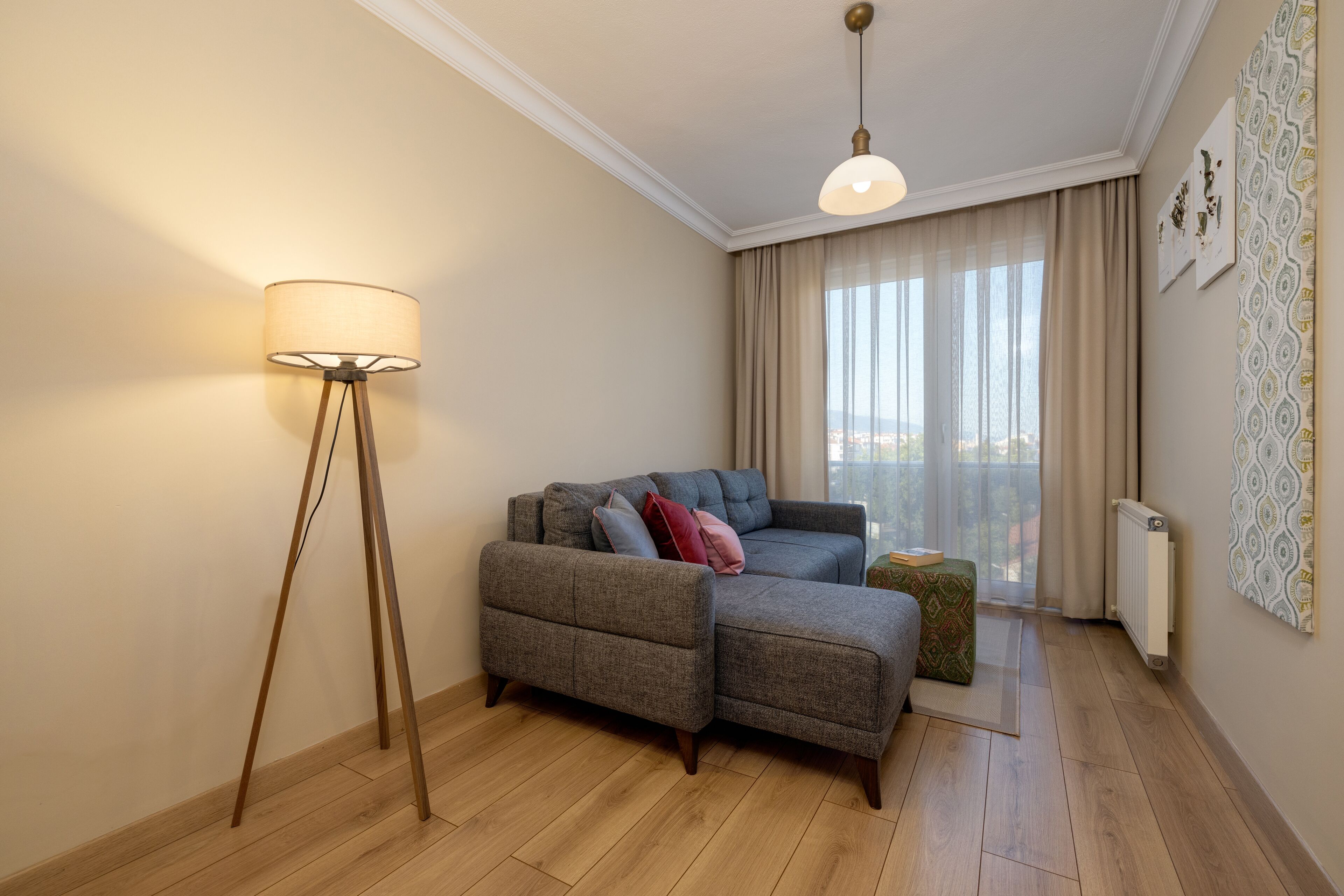Una sala de estar moderna con un sofá gris, una lámpara de pie y vistas a la ciudad a través de amplios ventanales.