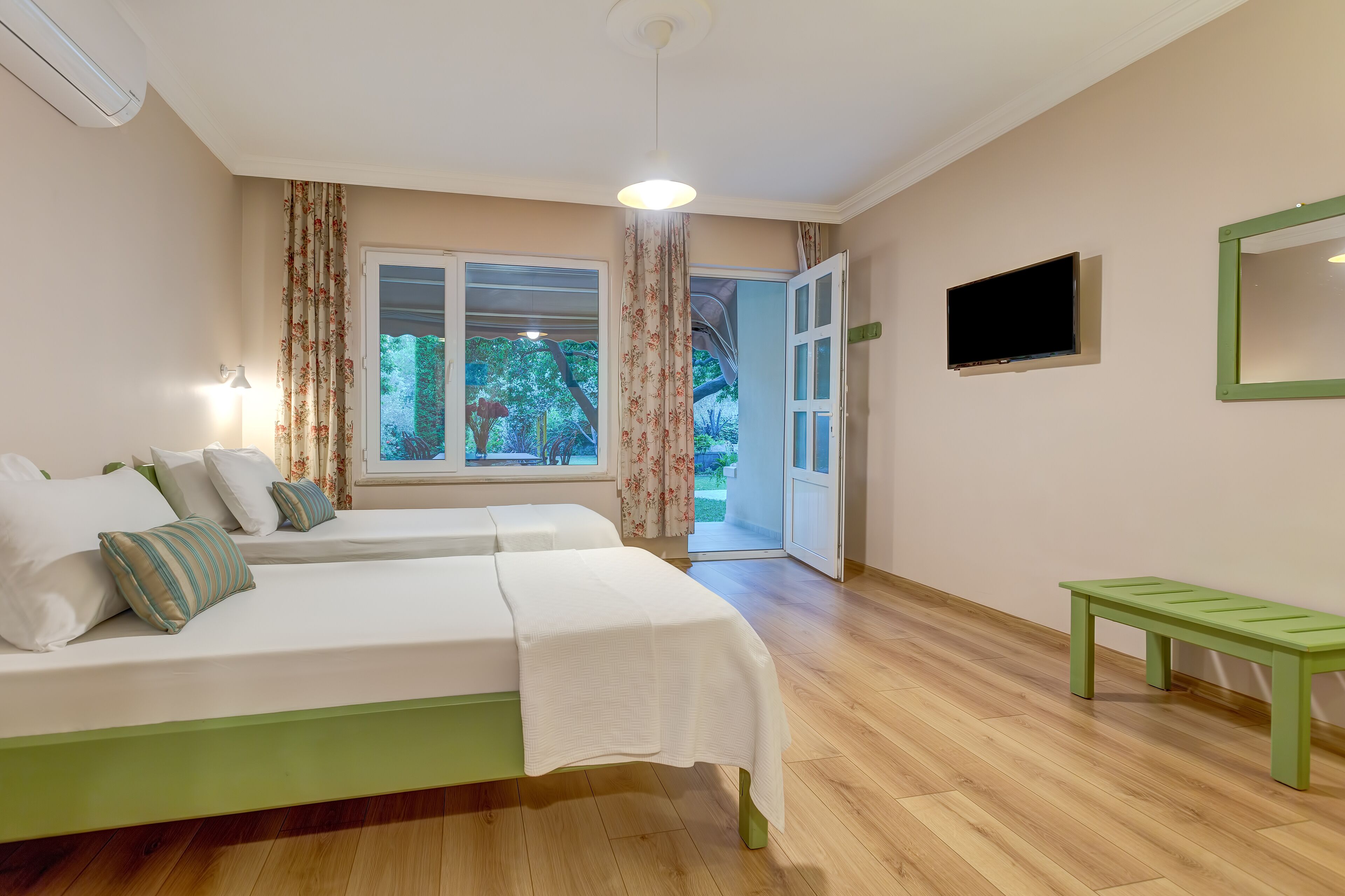 A room with two beds, a green bench, a TV, and a window with curtains.