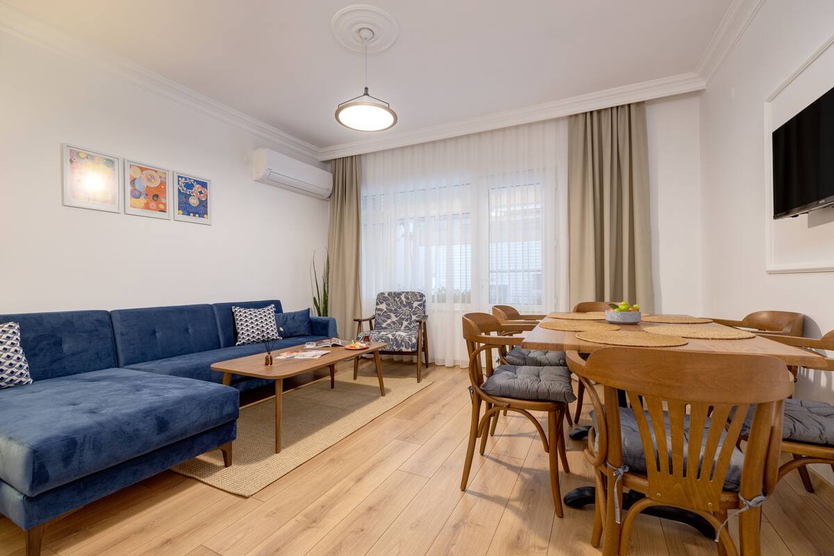 Una sala de estar moderna con un sofá azul, una mesa de comedor de madera y sillas.