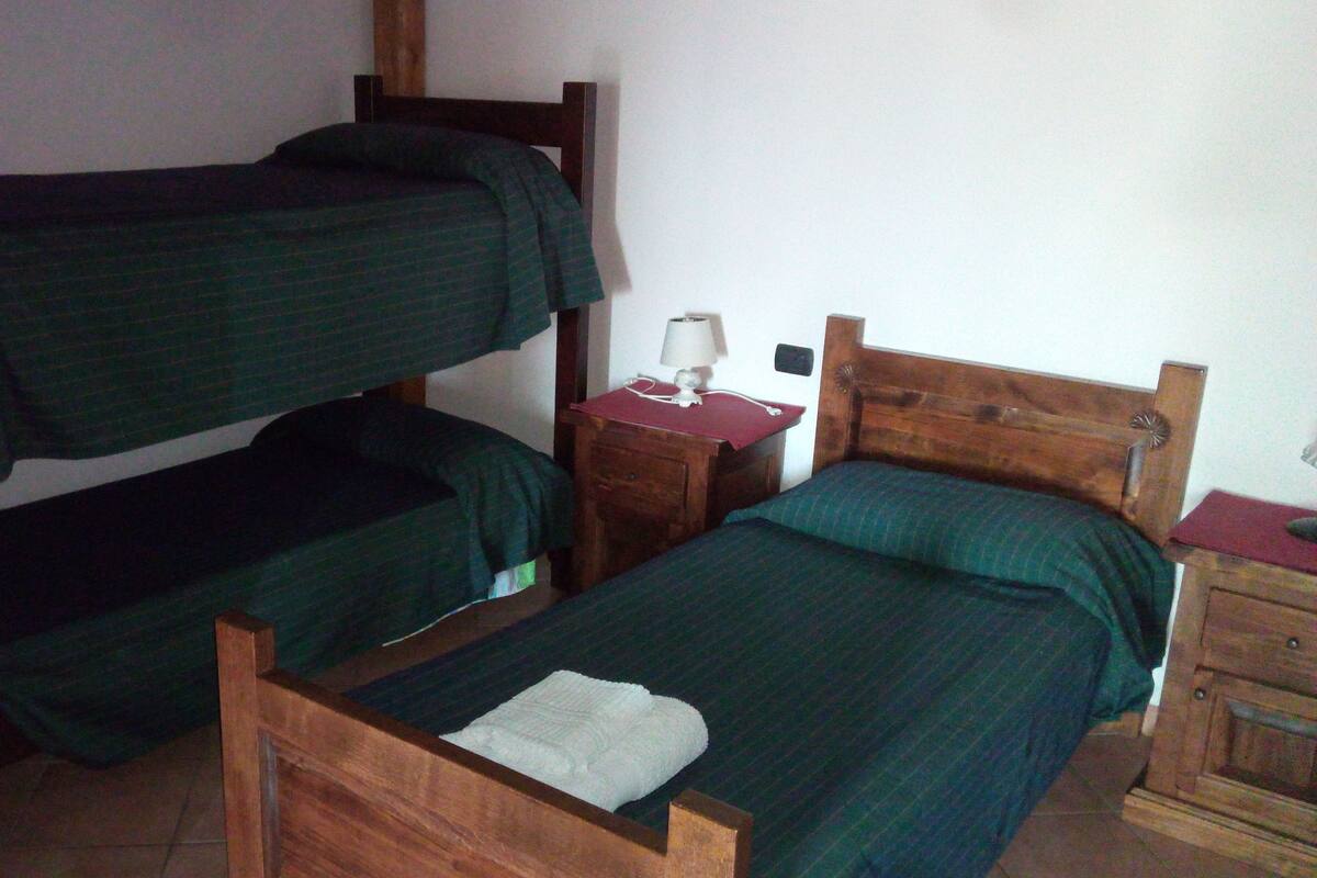 A room with two bunk beds, a wooden nightstand with a lamp, and a small wooden cabinet.