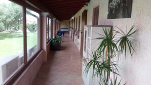 A covered corridor with large windows, potted plants, and a tiled floor. - Agriturismo Is Scalas (Assemini)
