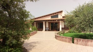 A building with a tiled roof, large windows, and a paved entrance area. - Agriturismo Is Scalas (Assemini)