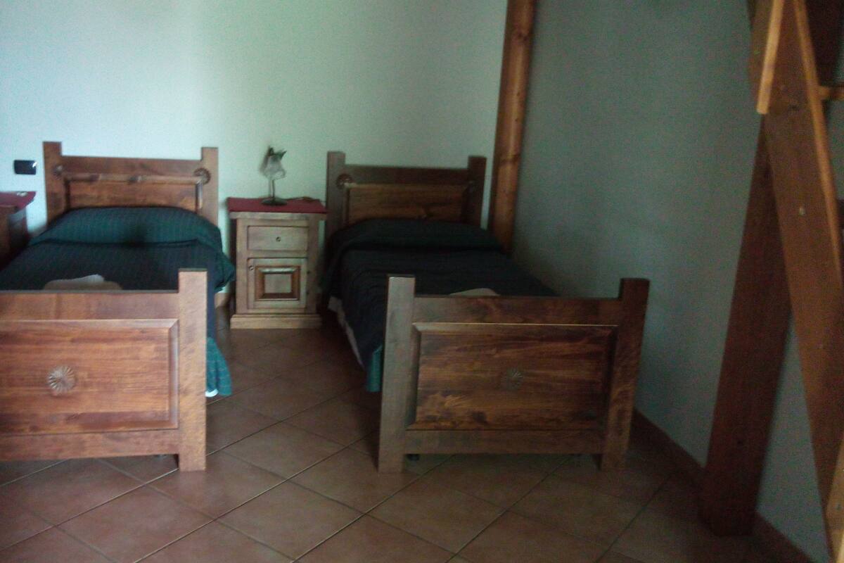 A small, dimly lit room with two wooden beds, a nightstand, and a dresser.