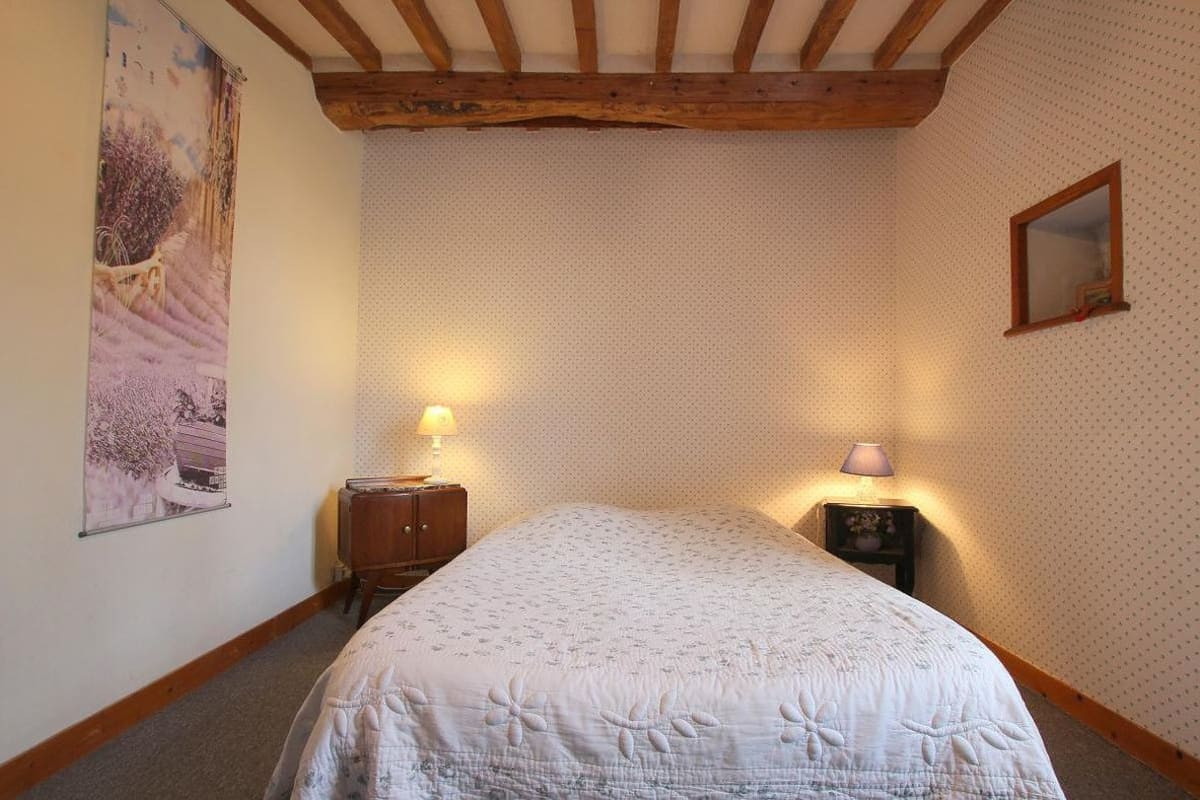 Een slaapkamer met een bed, twee nachtkastjes met lampen, een spiegel aan de muur en een poster.