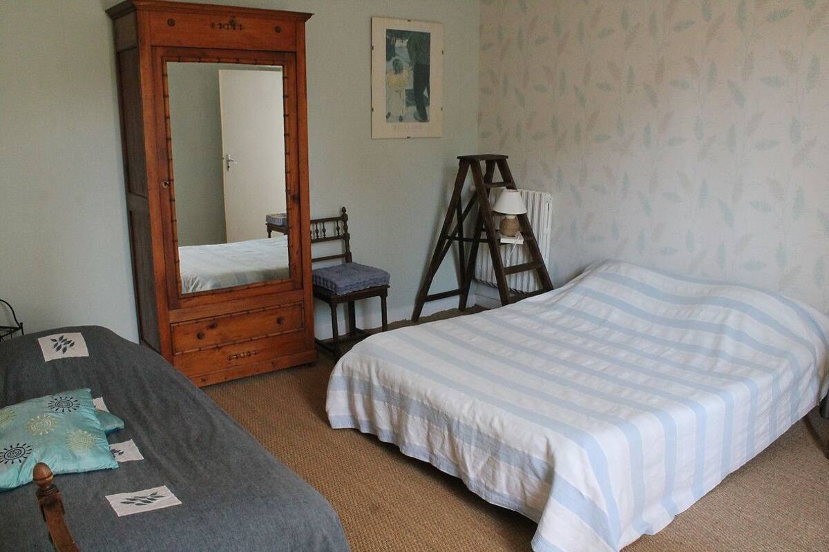 Een kamer met twee bedden, een houten garderobe, een ladder en een lijst met een afbeelding aan de muur.