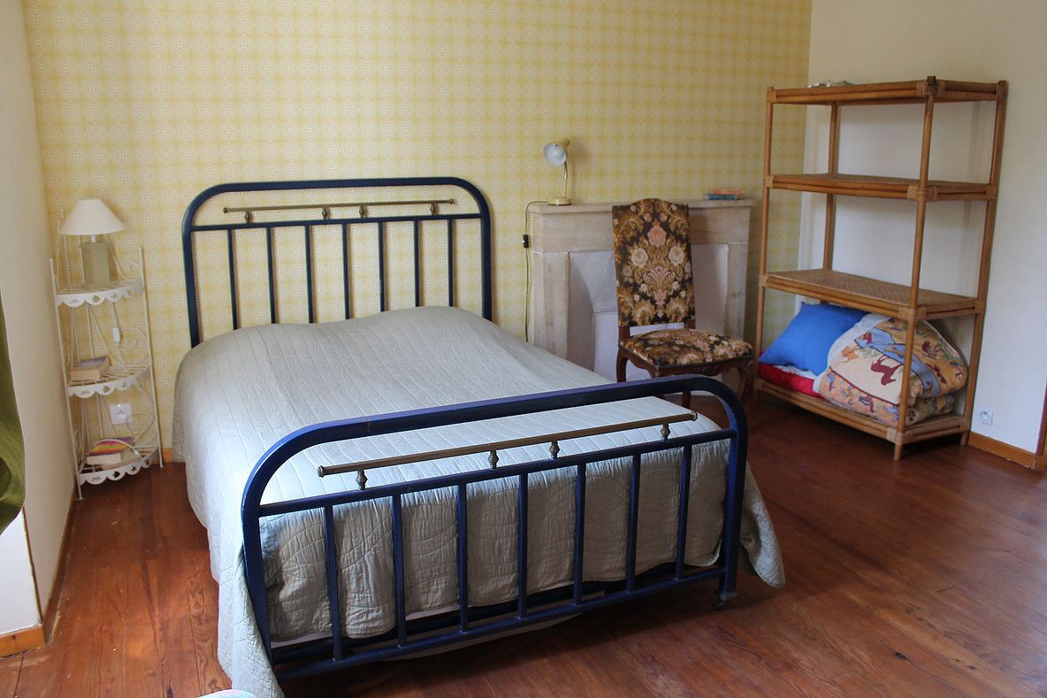 Une chambre avec un lit en métal, une chaise, une petite étagère en bois et un mur décoré d’un motif.