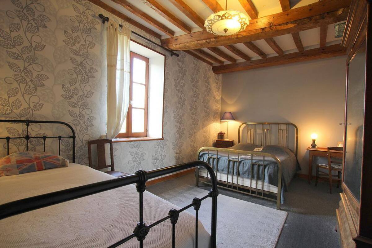 Een slaapkamer met twee bedden, een raam met gordijnen, een lamp en een houten plafond.