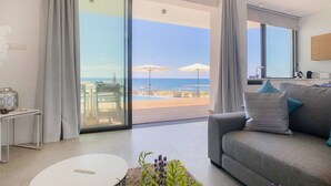 A modern living room with a grey sofa, a white coffee table, and a view of the beach and ocean through large sliding glass doors. - Villa Lara (Kouklia)