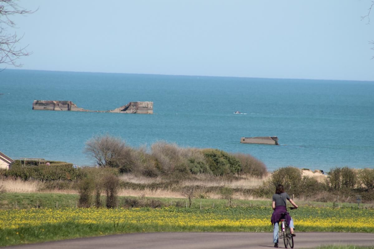 Una carretera costera con un ciclista, el mar a lo lejos y una estructura de piedra.