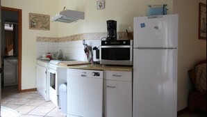 A compact kitchen with a microwave, stove, and refrigerator. There is a coffee maker on the counter, and a small sink is visible. - Gîte- La Ferme des Chataigniers (Vienne-en-Bessin)