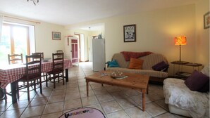 A living room with a dining table, chairs, a sofa, and a coffee table. - Gîte- La Ferme des Chataigniers (Vienne-en-Bessin)