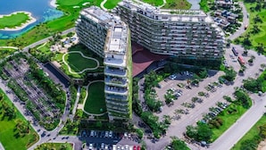 A modern hotel with a unique curved architecture, surrounded by well-maintained gardens and a parking area.