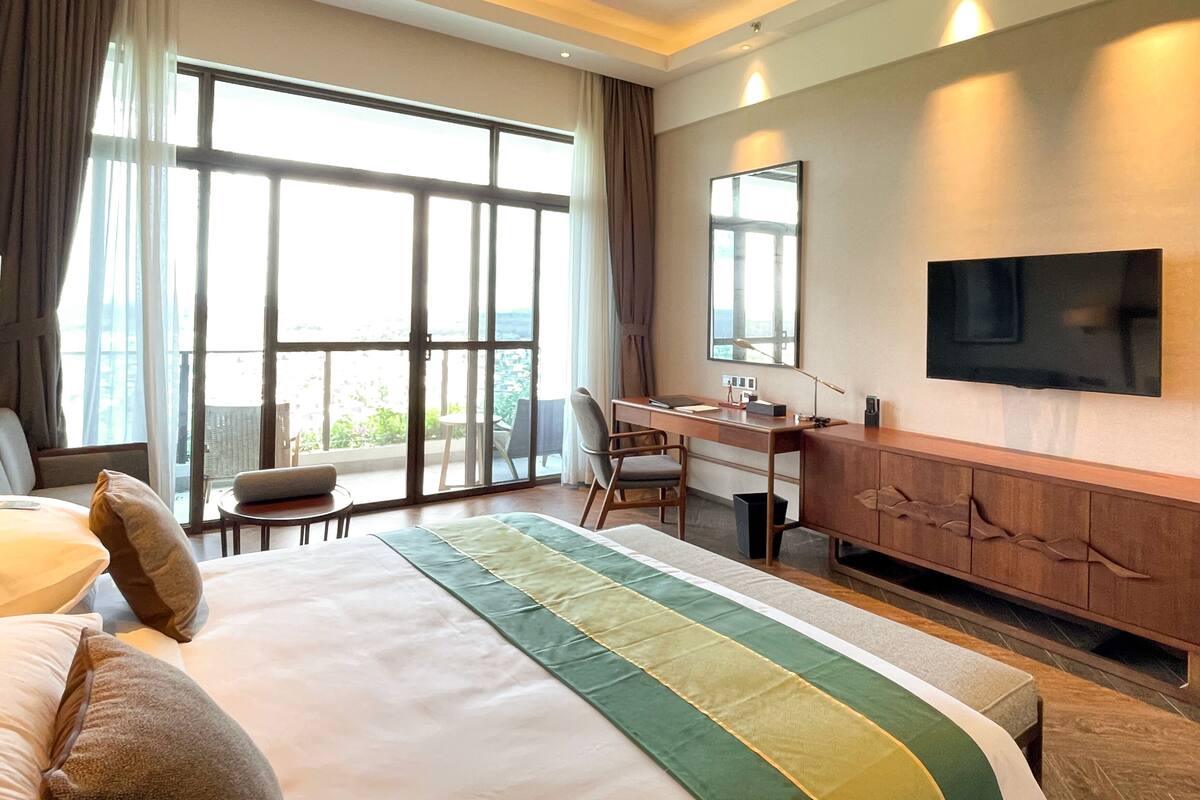 Habitación de hotel con una cama grande, un escritorio, una silla, un televisor y un balcón con vistas.