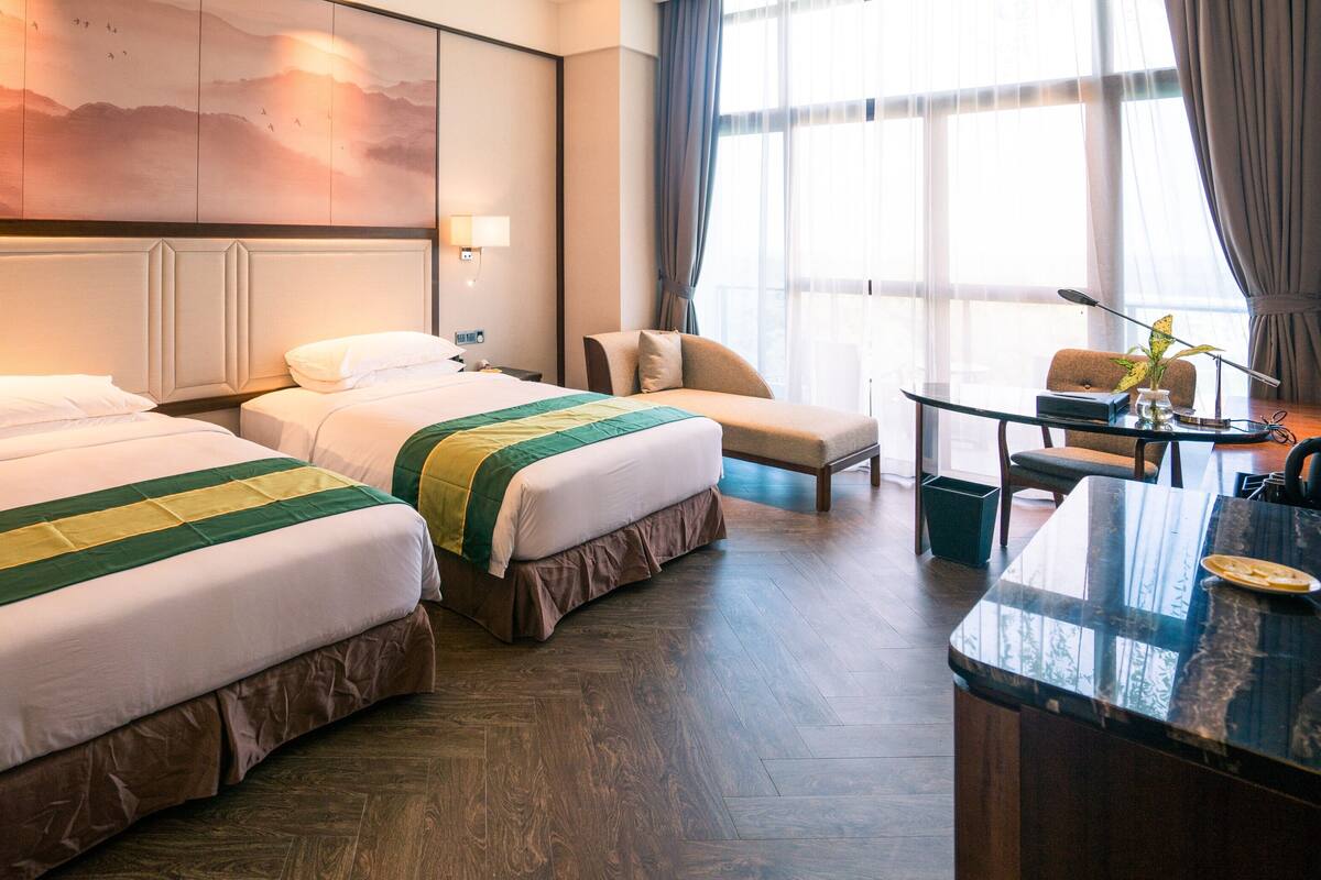 Habitación de hotel con dos camas, un escritorio y un amplio ventanal con cortinas.