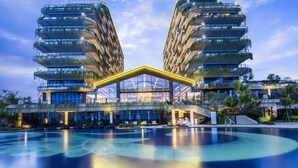 A modern hotel with two tall buildings, a central glass structure, and a swimming pool.