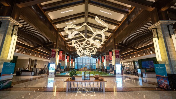 A spacious lobby with a high ceiling, a central seating area, and a large digital display.