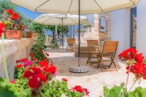 An outdoor patio with stone flooring, wooden chairs, and large umbrellas. - Feudo d'Arneo (Nardò)